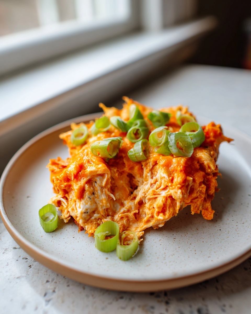 A scoop of creamy, cheesy buffalo chicken dip topped with fresh green scallions on a speckled plate.
