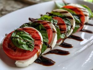 Close-up of sliced tomatoes, fresh mozzarella, and basil arranged beautifully for a caprese salad, drizzled with balsamic glaze.