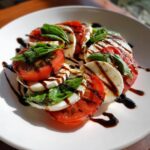 Close-up of a beautiful caprese salad featuring alternating slices of tomato, mozzarella, and basil, drizzled with dark balsamic glaze.