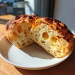 Cross-section view showing the open, airy crumb structure of cheesy sourdough english muffins.