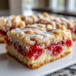 A close-up of a single square of cherry pie bars showing the thick cherry filling and crumb topping drizzled with white icing.