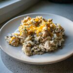 A close-up serving of creamy chicken wild rice casserole topped with melted cheddar cheese and fresh thyme.
