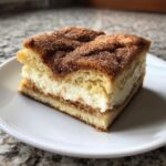 A square slice of churro cheesecake bars featuring a thick, creamy white layer and a cinnamon-sugar topping.