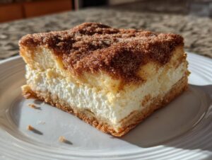 A thick slice of churro cheesecake bars with a creamy white filling and a cinnamon sugar topping.