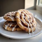 A stack of three soft cinnamon roll cookies drizzled generously with white vanilla icing.