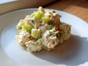 A mound of creamy cottage cheese tuna salad mixed with chopped celery served on a white plate.