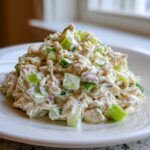 A mound of creamy cottage cheese tuna salad mixed with bright green celery and red onion chunks on a white plate.