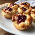 Close-up of golden baked cranberry brie bites made with puff pastry, served on a white plate.