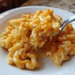 A spoonful of creamy, cheesy cottage cheese mac and cheese being lifted from a white plate.
