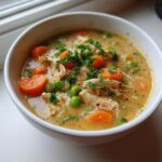 Close-up of creamy pot pie soup filled with shredded chicken, carrots, peas, and fresh parsley garnish.