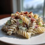 A serving of creamy ranch pasta salad made with rotini pasta, bacon bits, celery, and red onion on a white plate.