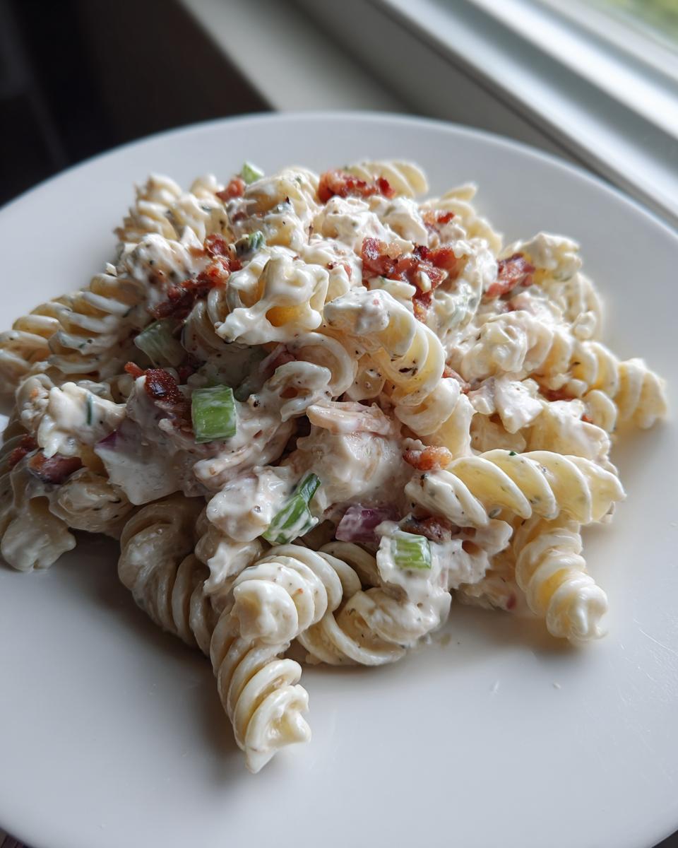 Close-up of a serving of ranch pasta salad featuring rotini pasta coated in creamy dressing, bacon bits, and green celery.