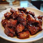 Close-up of tender crockpot steak bites coated in a thick, glossy, dark brown sauce and sprinkled with sesame seeds.