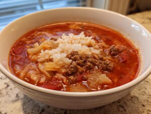 Close-up of a white bowl filled with rich, red cabbage soup, ground beef, and topped with white rice.