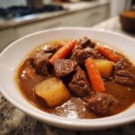 Close-up of tender chunks of beef stew with carrots and potatoes in a rich brown gravy.