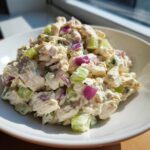 Close-up of a bowl filled with creamy high protein chicken salad mixed with diced celery and red onion.