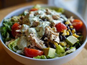 Close-up of a vibrant high protein salad featuring shredded chicken, black beans, corn, avocado, and tomatoes, topped with a creamy green dressing.