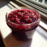 Close-up of a glass jar filled with rich, jewel-toned homemade christmas jam catching the sunlight.