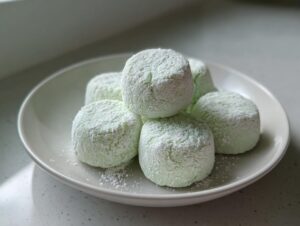 A small stack of light green cream cheese mints generously dusted with white powdered sugar on a white plate.
