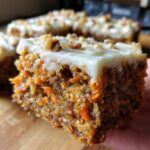 Close-up of a moist carrot cake bars slice topped with thick cream cheese frosting and chopped walnuts.