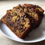 Three thick slices of moist chocolate chip banana bread stacked on a white plate.