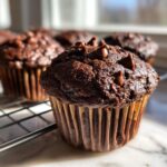 Close-up of a moist chocolate muffin topped with chocolate chips, resting on a cooling rack.