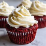 Close-up of a vibrant red velvet cupcakes topped with a generous swirl of white cream cheese frosting.