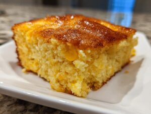 Close-up of a square slice of moist jiffy corn casserole with a golden, slightly caramelized top.