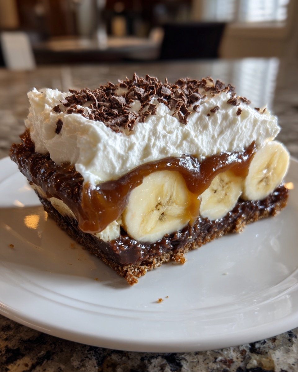 A decadent slice of no-bake banoffee pie featuring a biscuit base, bananas, caramel, and whipped cream topped with chocolate shavings.