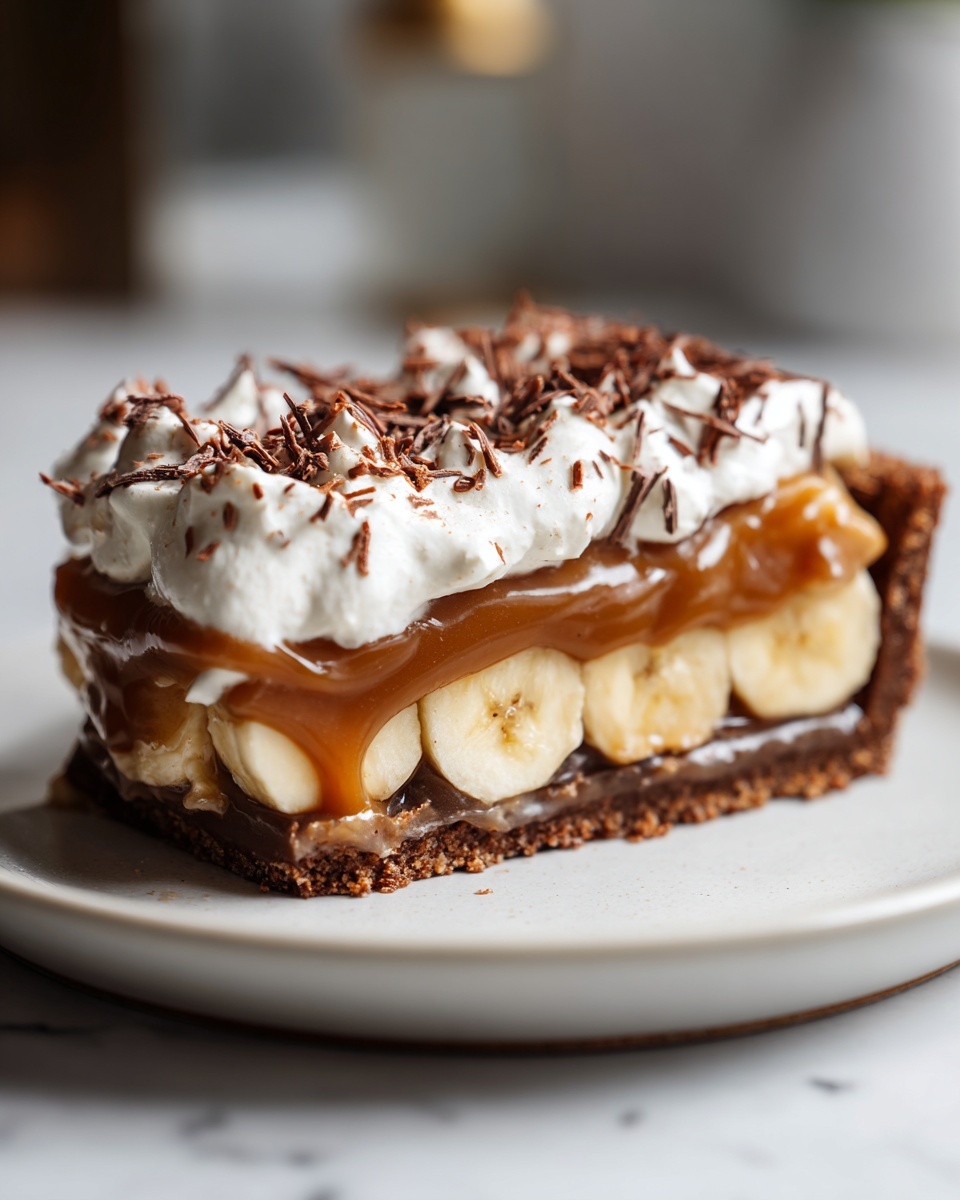 A close-up slice of no-bake banoffee pie showing layers of chocolate crust, bananas, toffee, and whipped cream with chocolate shavings.