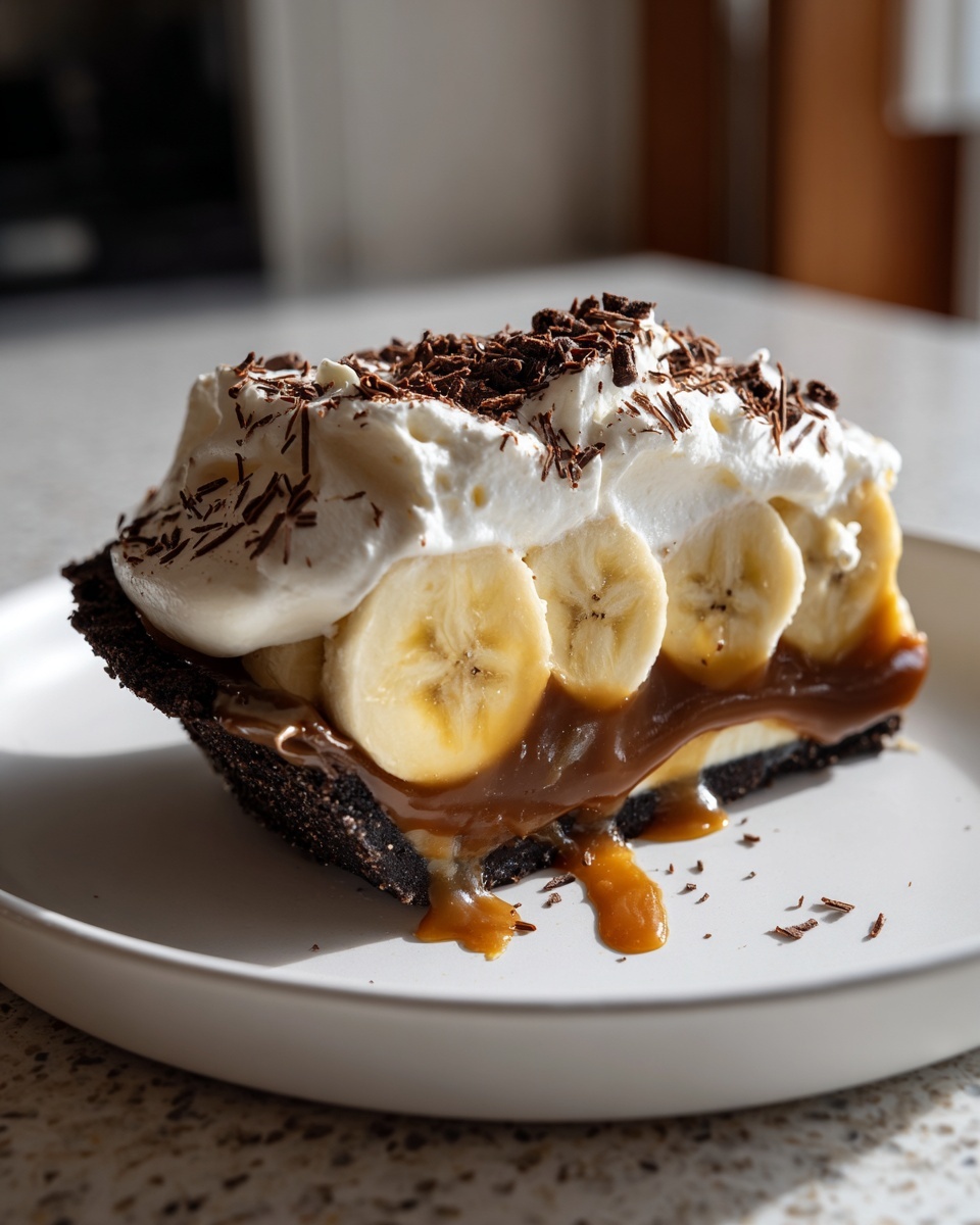 A decadent slice of no-bake banoffee pie featuring a dark crust, bananas, caramel, whipped cream, and chocolate shavings.