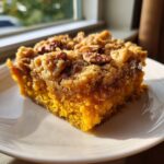 A close-up of a moist slice of pumpkin dump cake topped with a crunchy pecan streusel.