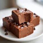 Close-up of rich, thick squares of salted caramel fudge topped with sea salt flakes and mini chocolate chips.