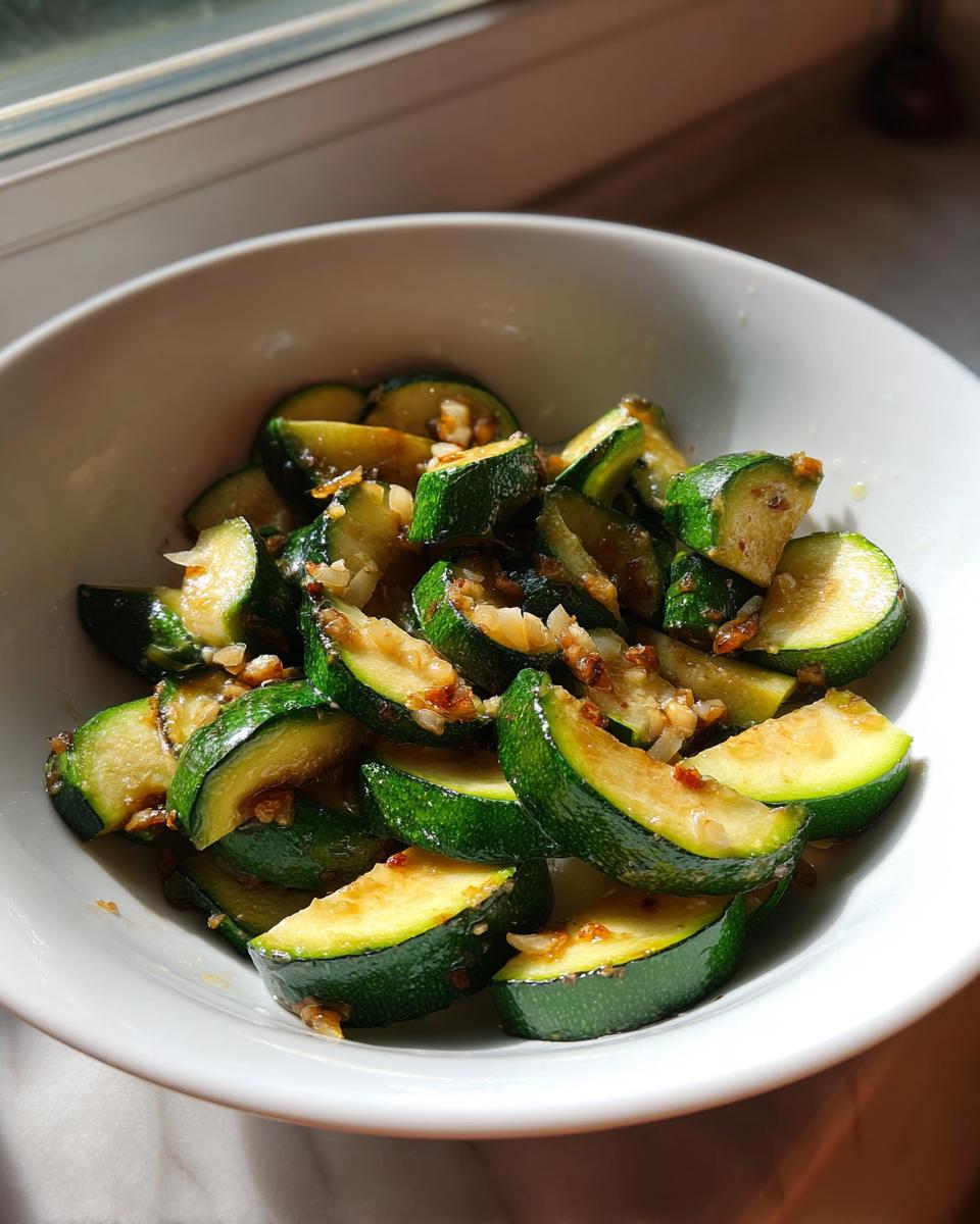 Close-up of bright green sauteed zucchini slices mixed with garlic pieces in a white bowl.