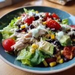 Close-up of a vibrant high protein salad featuring shredded chicken, avocado, black beans, corn, and tomatoes with a creamy dressing.