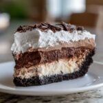 A decadent slice of Mississippi Mud Pie showing six distinct layers, topped with whipped cream and chocolate shavings.