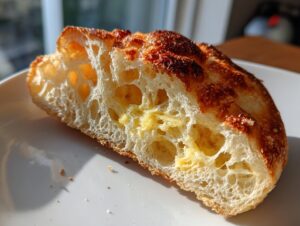 Close-up of a split sourdough english muffin showing open, airy crumb texture and melted butter.
