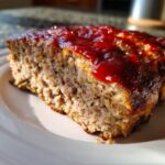 Close-up of a thick slice of stove top stuffing meatloaf topped with a shiny red glaze.