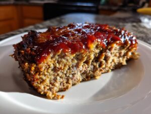 A thick slice of stove top stuffing meatloaf topped with a shiny red glaze on a white plate.