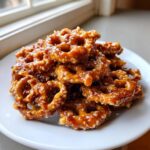 A close-up of a pile of crunchy, glazed toffee pretzels stacked high on a white plate.