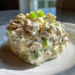 A mound of creamy chicken salad, featuring chunks of chicken, celery, and egg, garnished with green onion on a white plate.