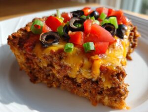 A close-up slice of amazing mexican pizza showing layers of seasoned meat, melted cheese, tomatoes, olives, and green onions.