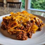 A close-up serving of Frito Pie featuring layers of seasoned ground beef and melted cheddar cheese over corn chips.