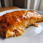 Close-up of a perfectly cooked piece of bang bang salmon, flaky inside and topped with a rich, orange-colored spicy sauce.