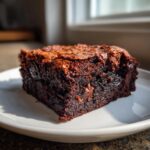 Close-up of a rich, dark, fudgy zucchini brownies slice on a white plate, showing melted chocolate chips.