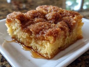Close-up of a warm, gooey slice of snickerdoodle cobbler with a thick cinnamon-sugar topping on a white plate.