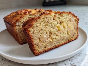 A close-up of two slices of moist Hawaiian banana bread, showing the texture and visible chunks of fruit and nuts.