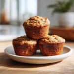 Three perfectly baked healthy greek yogurt banana muffins stacked on a small white plate.