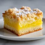 A single square of bright yellow lemon crumb bars with a thick, textured crumb topping dusted with powdered sugar.