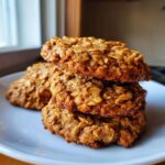 A stack of three golden brown low sugar applesauce oatmeal cookies resting on a white plate.